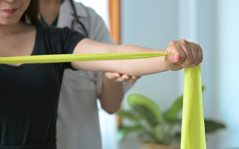 Physiotherapist assisting female patient do muscle rehabilitation exercising with elastic band.